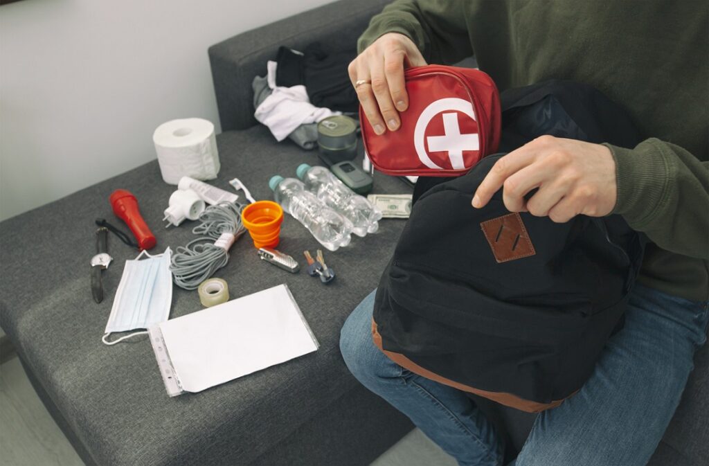 Young man packing the bag with documents, water,food, first aid kit and other items needed to survive