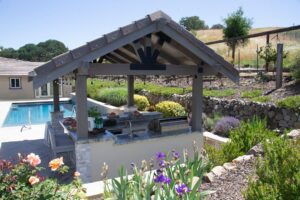 A wooden pergola has string lights over a seating area with an outdoor grill.